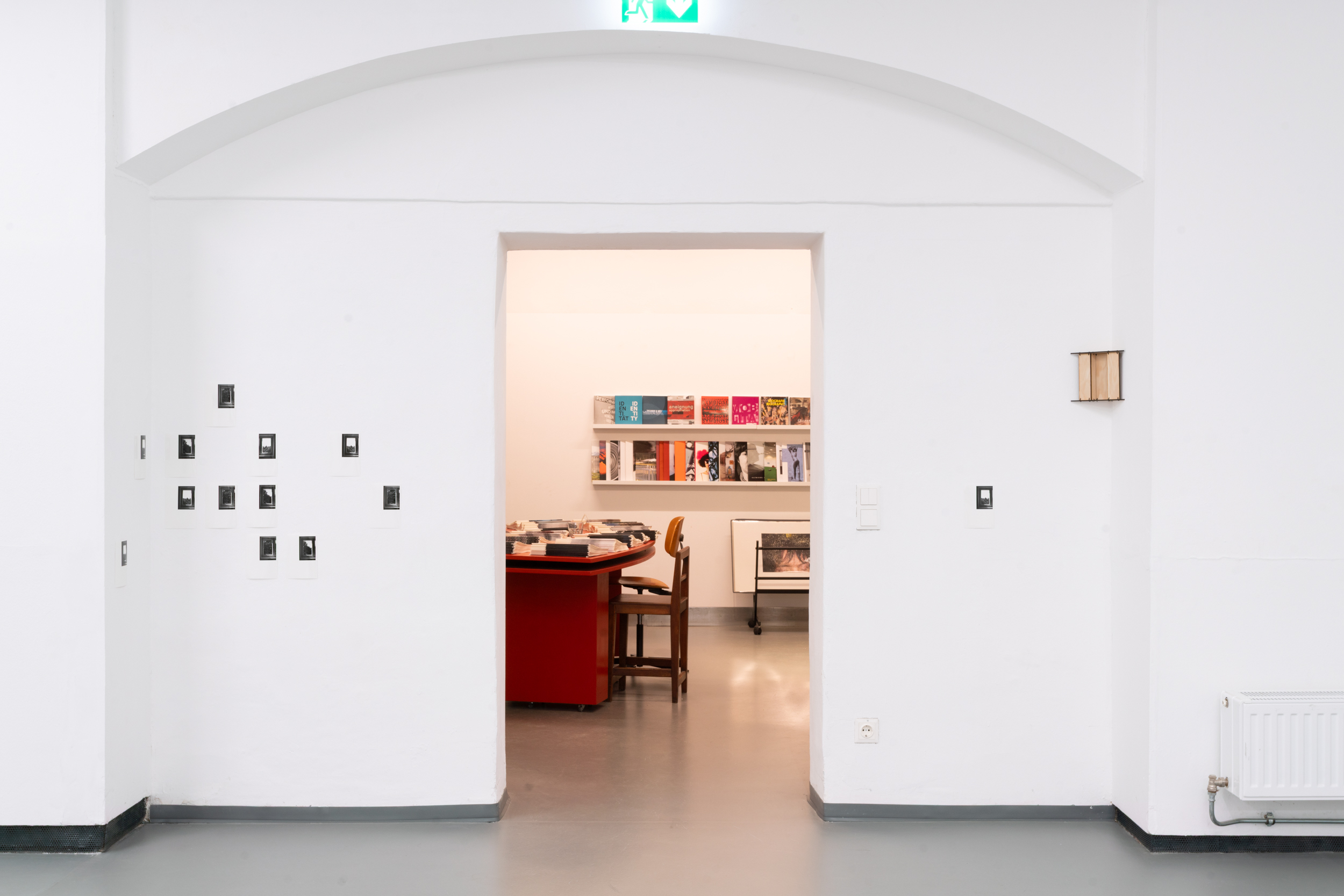 Stock für Stock, 2026 – Ausstellungsraum mit Rundbogendurchgang und Fotografiengruppe an der Wand.